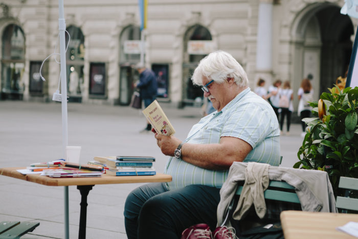 Ein älterer Mann sitzt auf einem Stuhl und liest die Broschüre mit dem Titel Kultur Inklusiv.