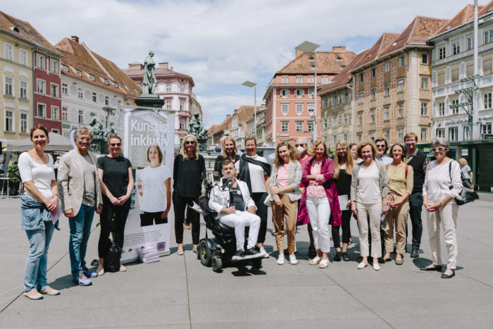 Auf einem Gruppenfoto am Grazer Hauptplatz stehen etwa zwanzig Männer und Frauen und im Vordergrund ein Mann in einem Rollstuhl.