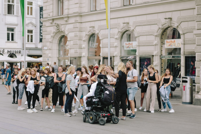 Eine Gruppe von Jugendlichen und ein Mann in einem Rollstuhl tanzen gemeinsam vor dem Grazer Rathaus