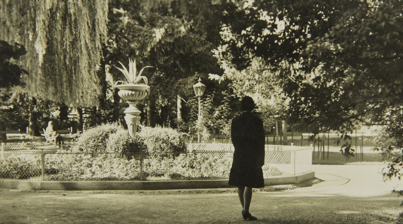 Eine Frau ist von hinten zu sehen, die vor einem Brunnen im Grazer Stadtpark steht. Im Brunnen befinden sich Pflanzen. Das Foto ist schwarzweiß und wurde 1930 gemacht.
